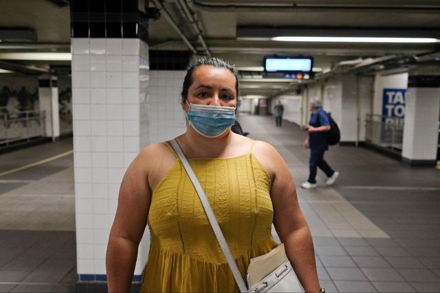 A woman wearing a mask stands in a subway station